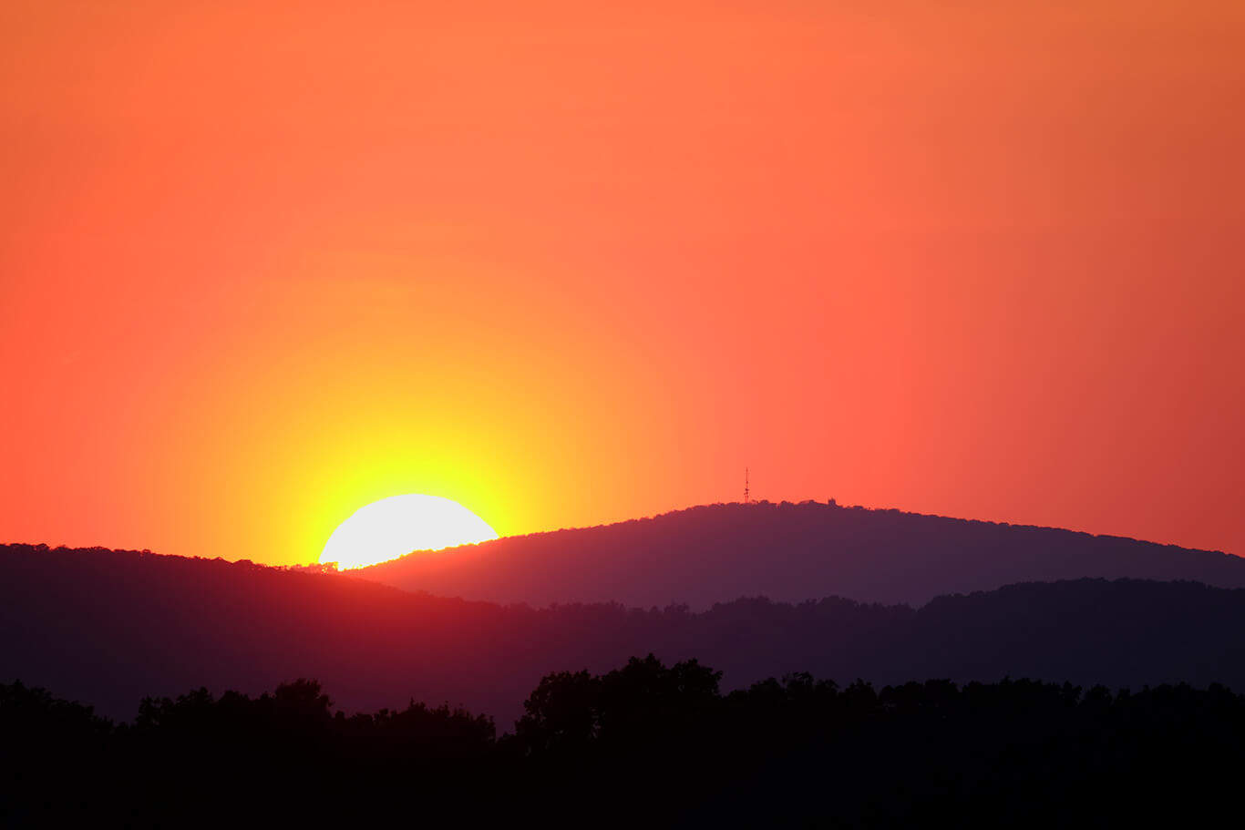 a landscape of the sun going below mountains
