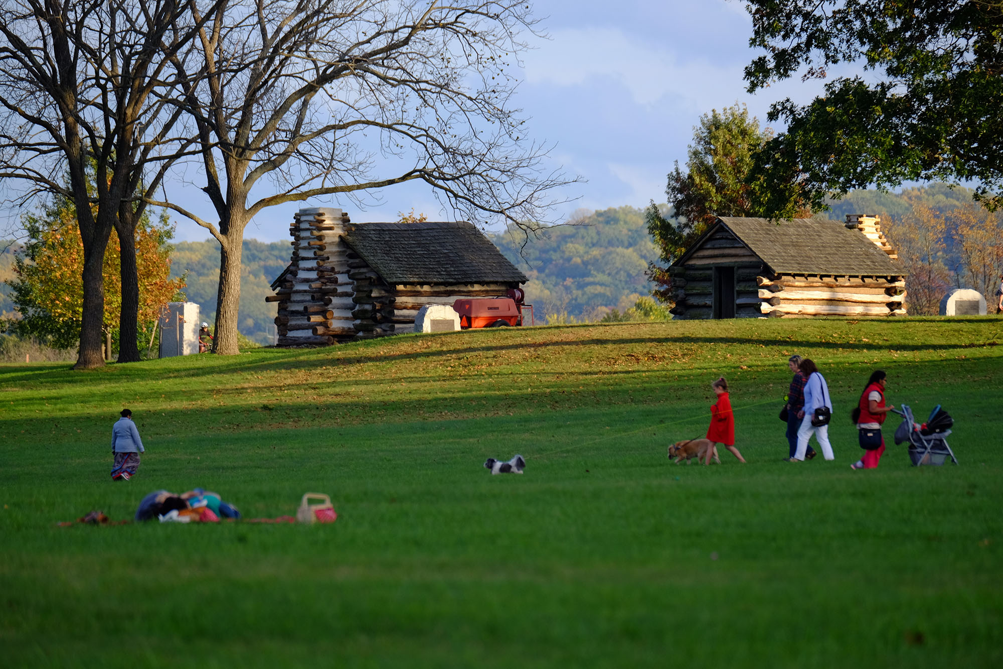 Log cabins set amongst hills while people in the foreground walk